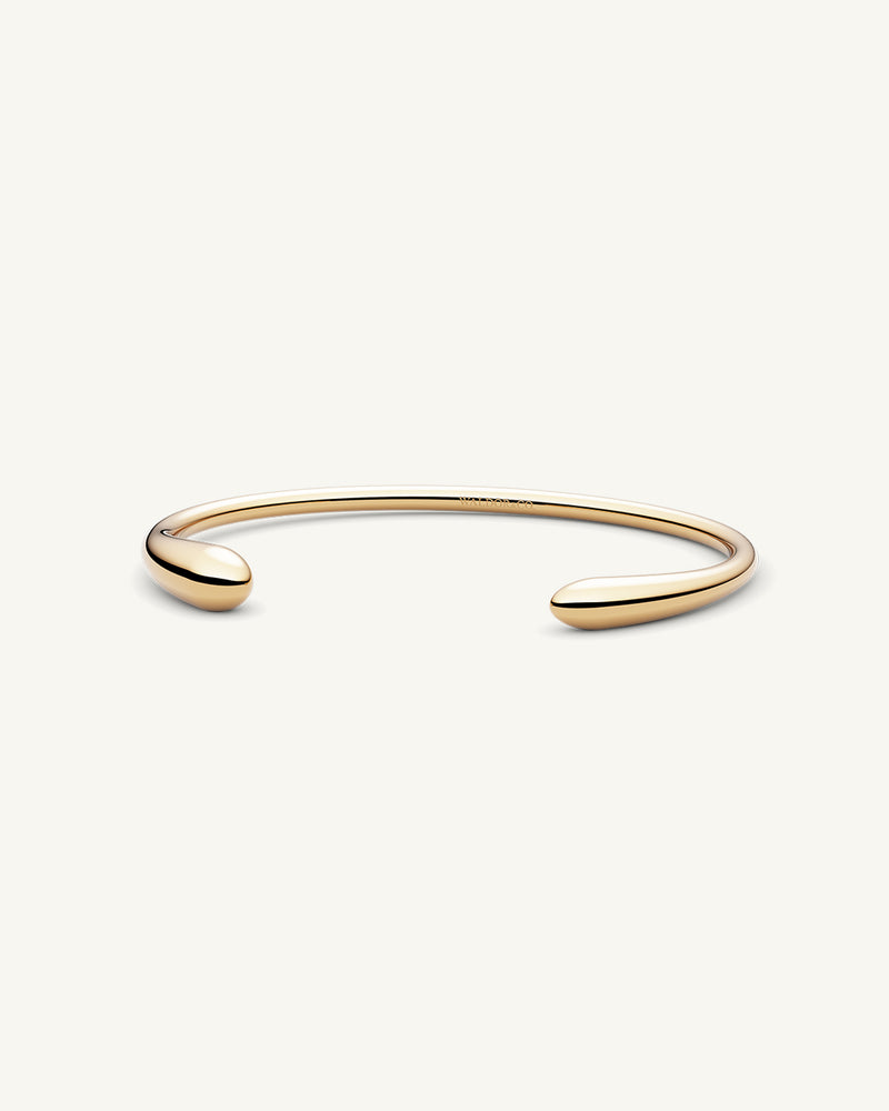 A polished stainless steel bangle in 14k gold from Waldor & Co. One size. The model is Teardrop Bangle Polished