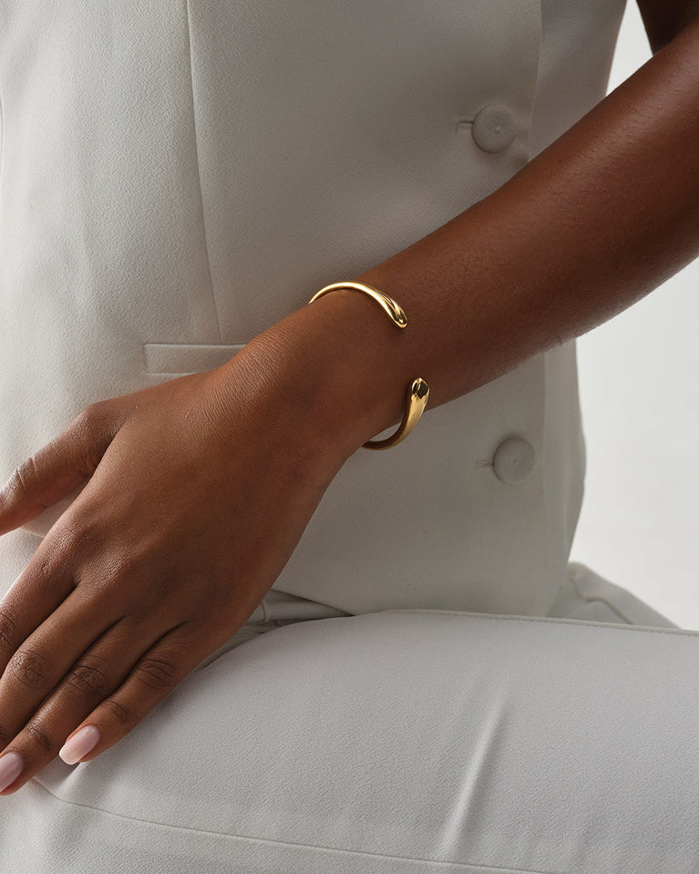 A polished stainless steel bangle in 14k gold from Waldor & Co. One size. The model is Teardrop Bangle Polished