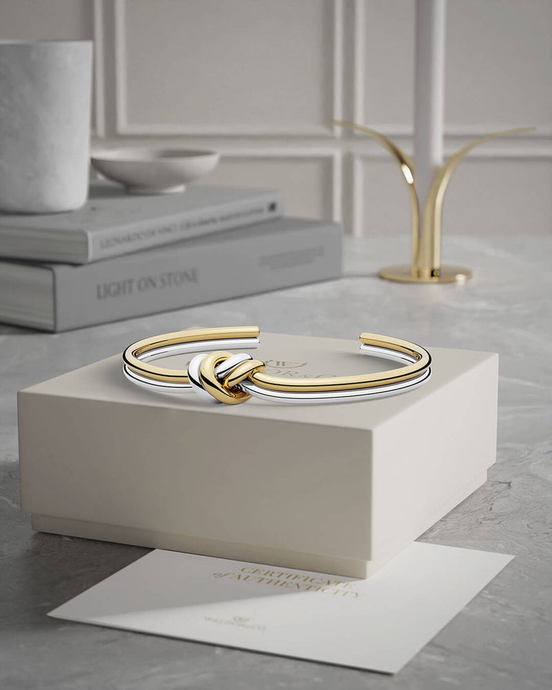 A polished stainless steel bangle in 14k gold from Waldor & Co. One size. The model is Dual Knot Bangle.